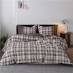 a bed with plaid comforter and pillows in a white room next to a lamp