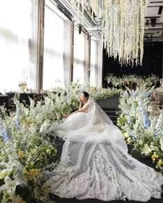 a woman in a wedding dress sitting on the ground surrounded by flowers