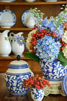 blue and white vases with flowers in them on a table next to other plates