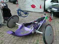 an upside down purple bike on the ground next to some parked cars and people looking at it