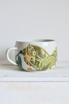 a cup with fish painted on it sitting on top of a shelf next to a wall