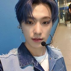 a young man with blue hair wearing a headset and denim jacket in an airport