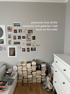 a room filled with lots of books on top of a wooden floor next to a white dresser