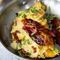 a metal bowl filled with bacon and cheese on top of a table next to bread