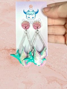 a pair of pink and green bird earrings on a card with a hand holding it