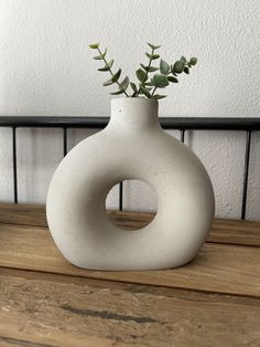 a white vase sitting on top of a wooden table next to a plant in it