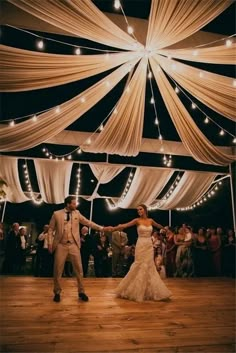 a bride and groom dancing under a tent with lights on the ceiling at their wedding reception