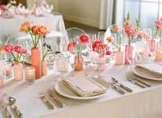 the table is set with pink and orange flowers in vases, candles, and plates