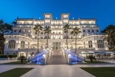 a large white building with lots of windows and palm trees in front of it at night