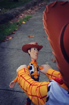 a toy is posed as a man in a cowboy hat and orange pants with his arm around another toy