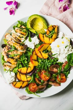 a white plate topped with chicken, rice and veggies next to a sliced avocado