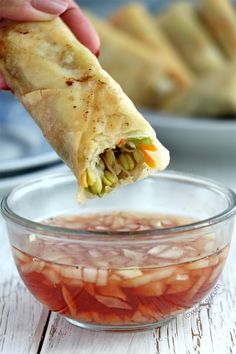 a hand holding a burrito over a bowl filled with sliced carrots and onions