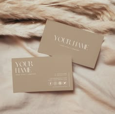 two business cards sitting on top of a bed next to a fur covered comforter