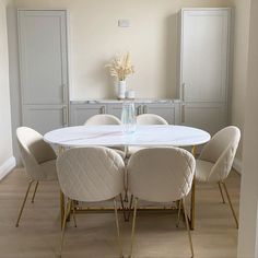 a dining room table with white chairs and a vase on top of it in front of some cupboards