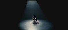 a woman is sitting in the middle of a dark room with light coming from behind her