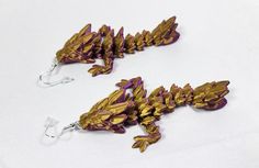 two gold and purple dragon earrings are on a white surface, one is dangling from a hook