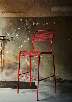 a red chair sitting in front of a wall with peeling paint on the walls and floor