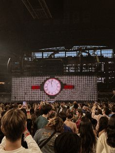 a large group of people standing in front of a stage with a clock on it