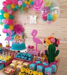 a table filled with lots of colorful desserts and balloons in the shape of flamingos