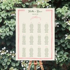 an easel with a seating chart on it in front of some bushes and flowers