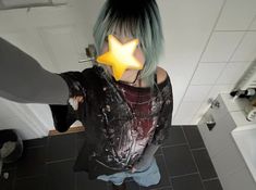 a person with green hair and a yellow star on their face is standing in a bathroom