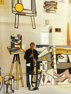 a man is standing in front of some art work and holding a paintbrush while looking at it