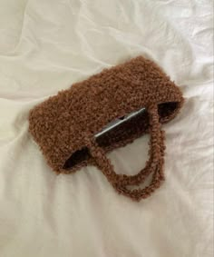 a brown purse laying on top of a white bed next to a pair of scissors