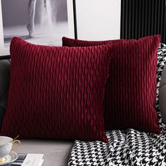 two red pillows sitting on top of a couch next to a cup and saucer