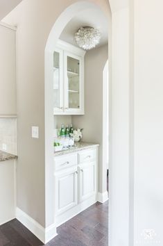 a white kitchen with an arched doorway leading into the dining room and living room area