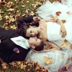 a bride and groom laying on the ground in autumn leaves