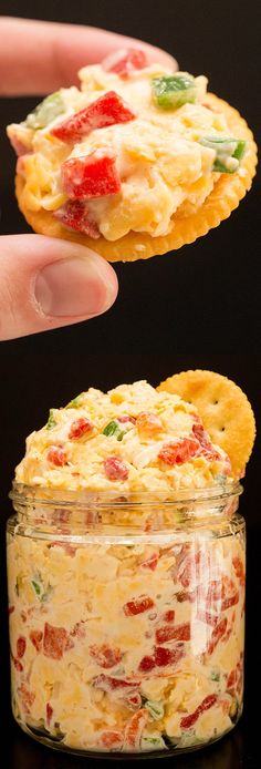 a hand holding a cracker over a jar filled with food