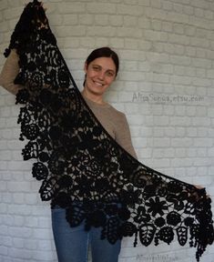 a woman wearing a black lace shawl in front of a white brick wall smiling at the camera