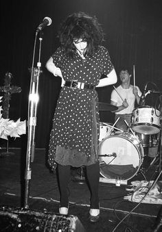 a woman with long hair standing in front of a microphone on stage next to other people