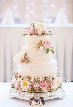 a wedding cake with pink and yellow flowers on top is displayed in front of a white table cloth