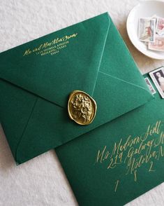 a green envelope with a gold wax stamp on it next to some stamps and a plate