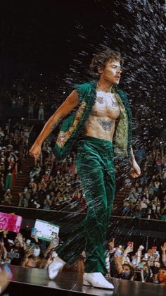 a man in green pants and white sneakers walking on a stage with water splashing over his head