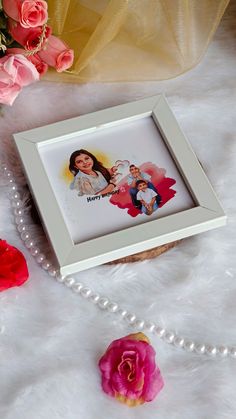 a white frame sitting on top of a table next to pink roses and a pearl necklace