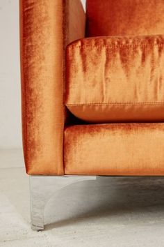 an orange velvet chair sitting on top of a white floor