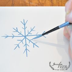 someone is drawing a snowflake on a piece of paper with a brush and watercolor pencil