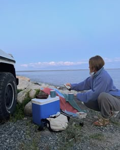 a woman is setting up her camping gear on the rocks by the water's edge