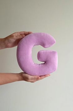 a person holding a purple letter shaped pillow in their hand with the letter g on it