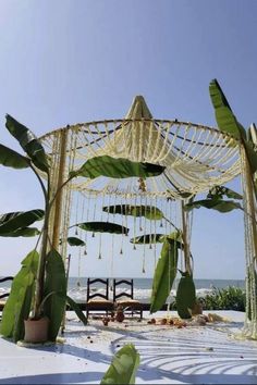 an outdoor wedding setup on the beach with flowers and greenery hanging from it's roof