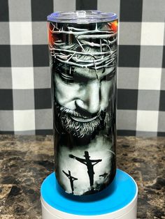 a glass with jesus on it is sitting on a blue stand in front of a black and white checkered wall