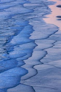 an ocean beach with waves coming in to shore and the sky reflecting on the sand