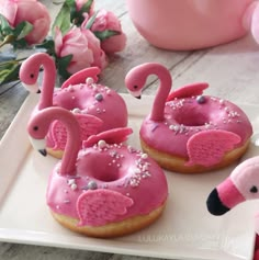 pink flamingo donuts with sprinkles are on a plate next to flowers