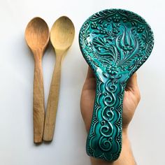 a hand holding a spoon and wooden spoon rest next to an ornate design on a green plate