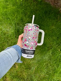 a person holding a coffee cup in their hand on the grass with flowers all over it