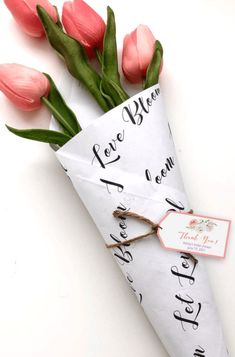 pink tulips are wrapped in paper and tied to a white envelope with the words love bloom written on it