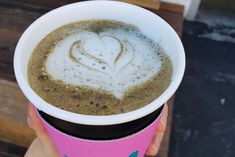 a person holding up a cup of coffee with a heart drawn on the foam in it