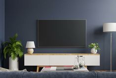 a flat screen tv mounted on the wall in a living room with blue walls and white furniture